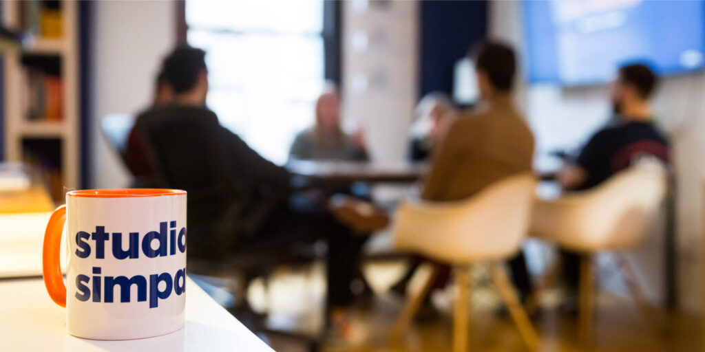 Studio Simpatico team in the conference room behind a Simpatico mug