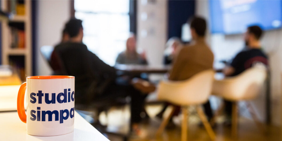 Studio Simpatico team in the conference room behind a Simpatico mug